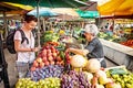 Young tourist woman buying fresh fruit from old woman at market